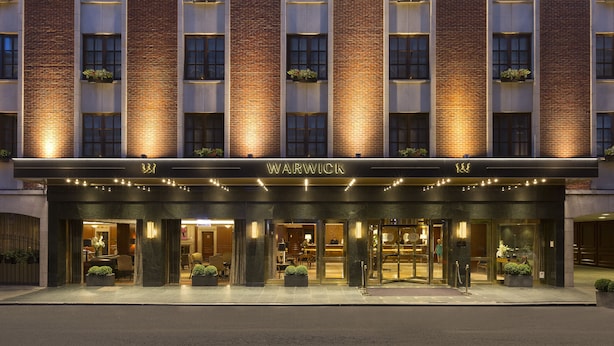 Entrada de hotel con fachada de ladrillo, ventanas iluminadas y un letrero que dice "WARWICK".