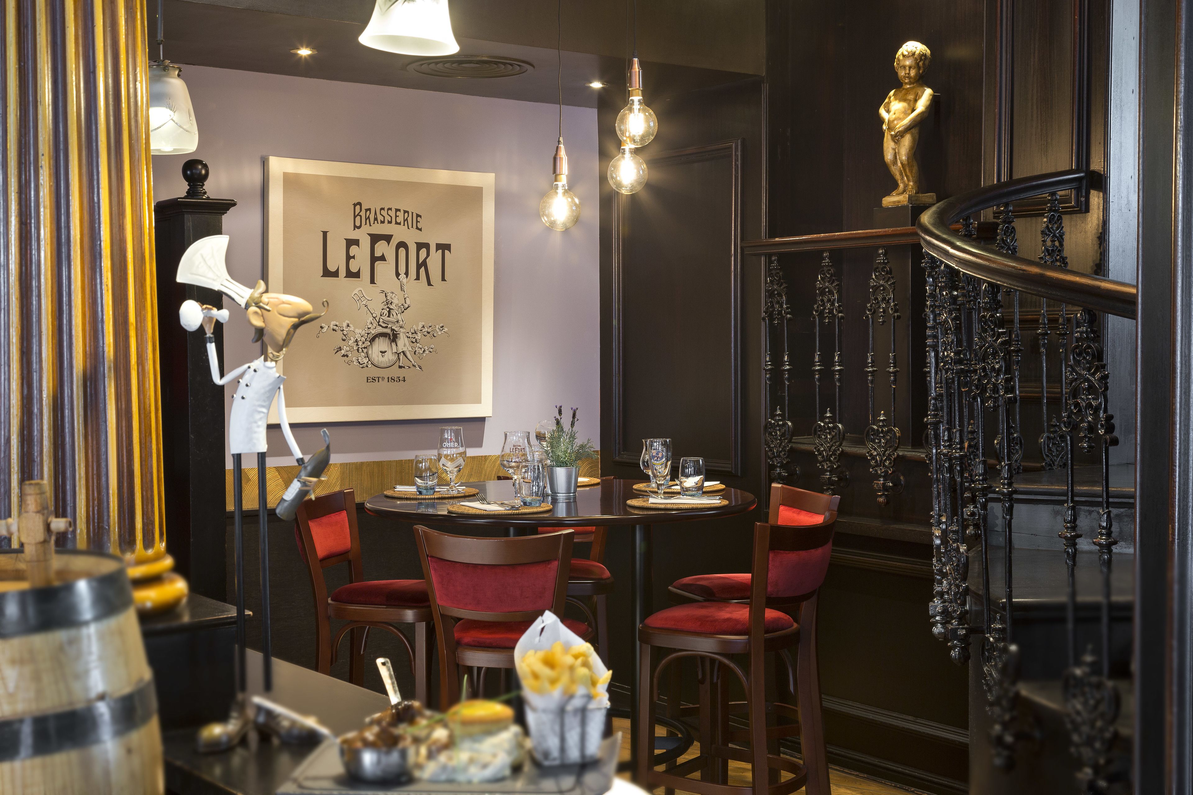 A restaurant interior with a vintage decor, including a brass sign, elegant chairs, and a staircase with ornate railings.