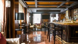 Zona de bar con suelo de madera pulida, asientos de cuero y barra con diferentes botellas.