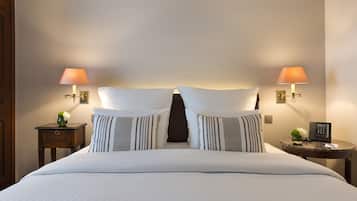 Una cama bien hecha con sábanas blancas y almohadas a rayas, flanqueada por dos mesitas de noche con lámparas y un pequeño jarrón de flores.