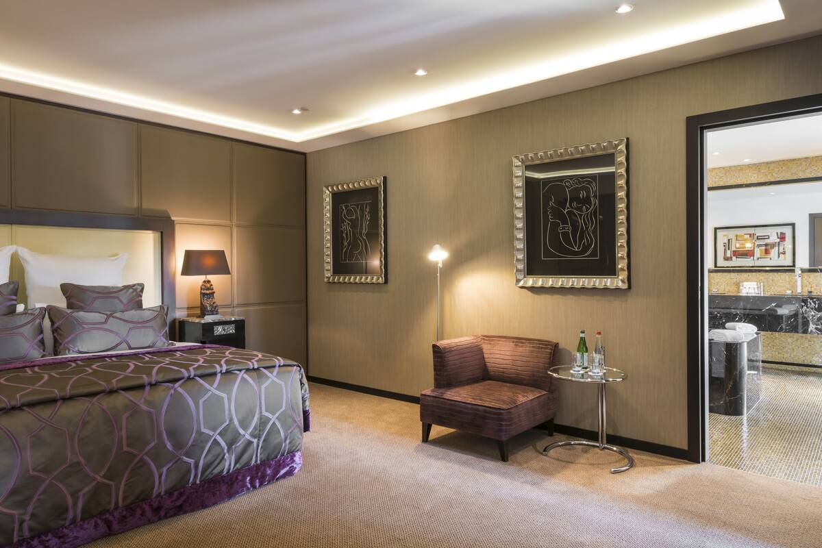 A hotel room with a large bed, a small armchair, a side table, and a mirror.