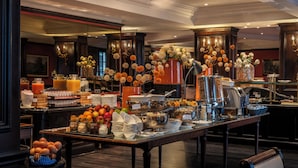 Una mesa de buffet con diversos alimentos y bebidas, una máquina de café y flores decorativas.