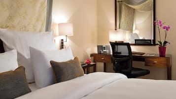 Une chambre d’hôtel comprenant un lit, deux tables de chevet, un bureau avec une chaise, un miroir et une plante en pot.