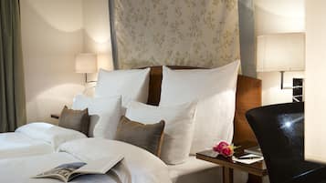 A hotel room with a neatly made bed, a bedside table with a lamp, a chair, and a small table with a flower vase.