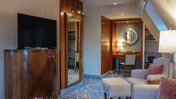 Habitación de hotel con televisión, armario de madera, zona de comedor con mesa y sillas, espejo y lámpara.