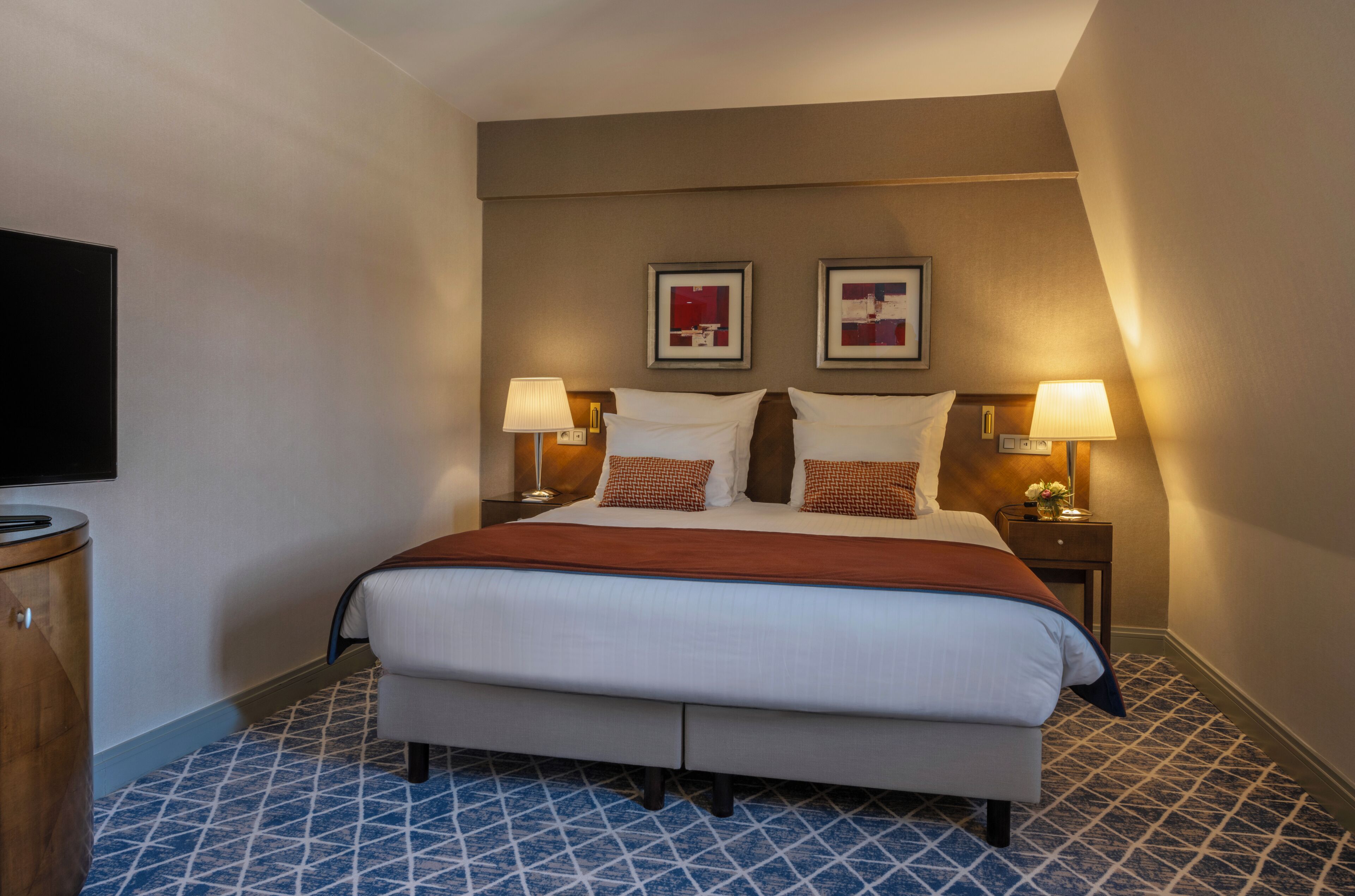Habitación de hotel con una cama grande, dos lámparas de noche, un televisor de pantalla plana y un suelo estampado.