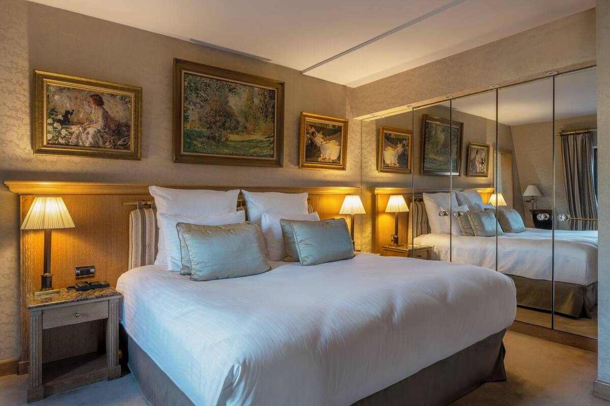 A hotel room with a large bed, two bedside tables with lamps, a mirror, and three framed artworks on the wall.