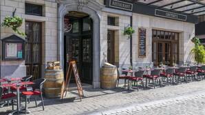 Un espacio al aire libre con mesas y sillas, un barril de madera y un cartel anunciador frente a un restaurante.