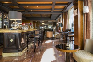 Een bar met een gepolijste marmeren vloer, donkerhouten lambrisering en een lange bar achtergrond met een ronde tafel en stoelen.