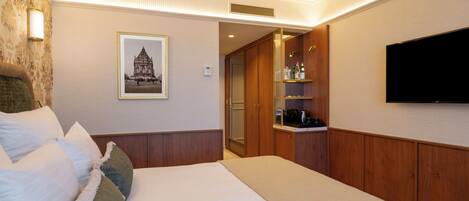 A hotel room with a bed, a television, a framed picture on the wall, and a minibar.