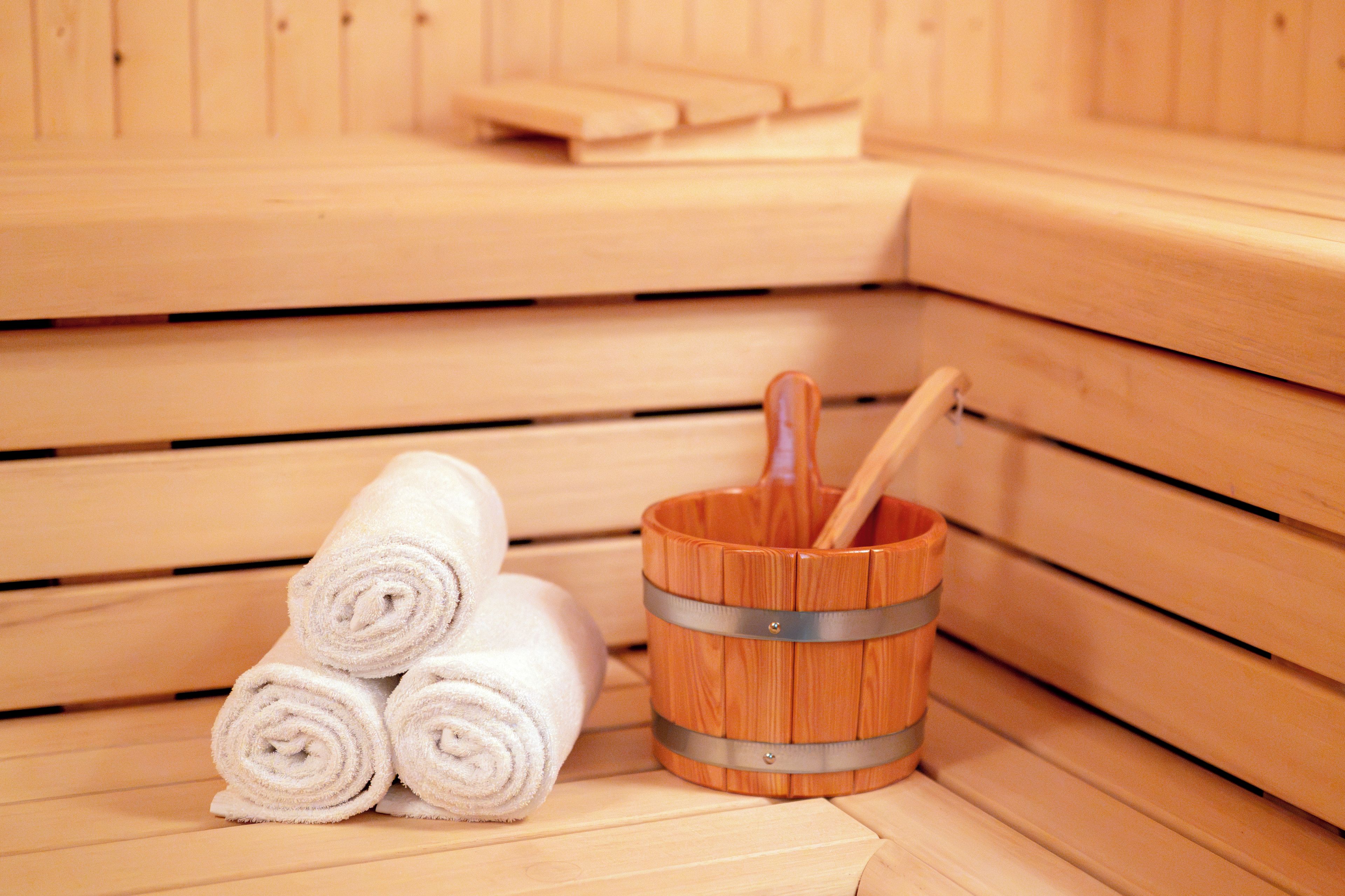 Een sauna met houten banken, een houten emmer met een houten klopper en opgerolde handdoeken.