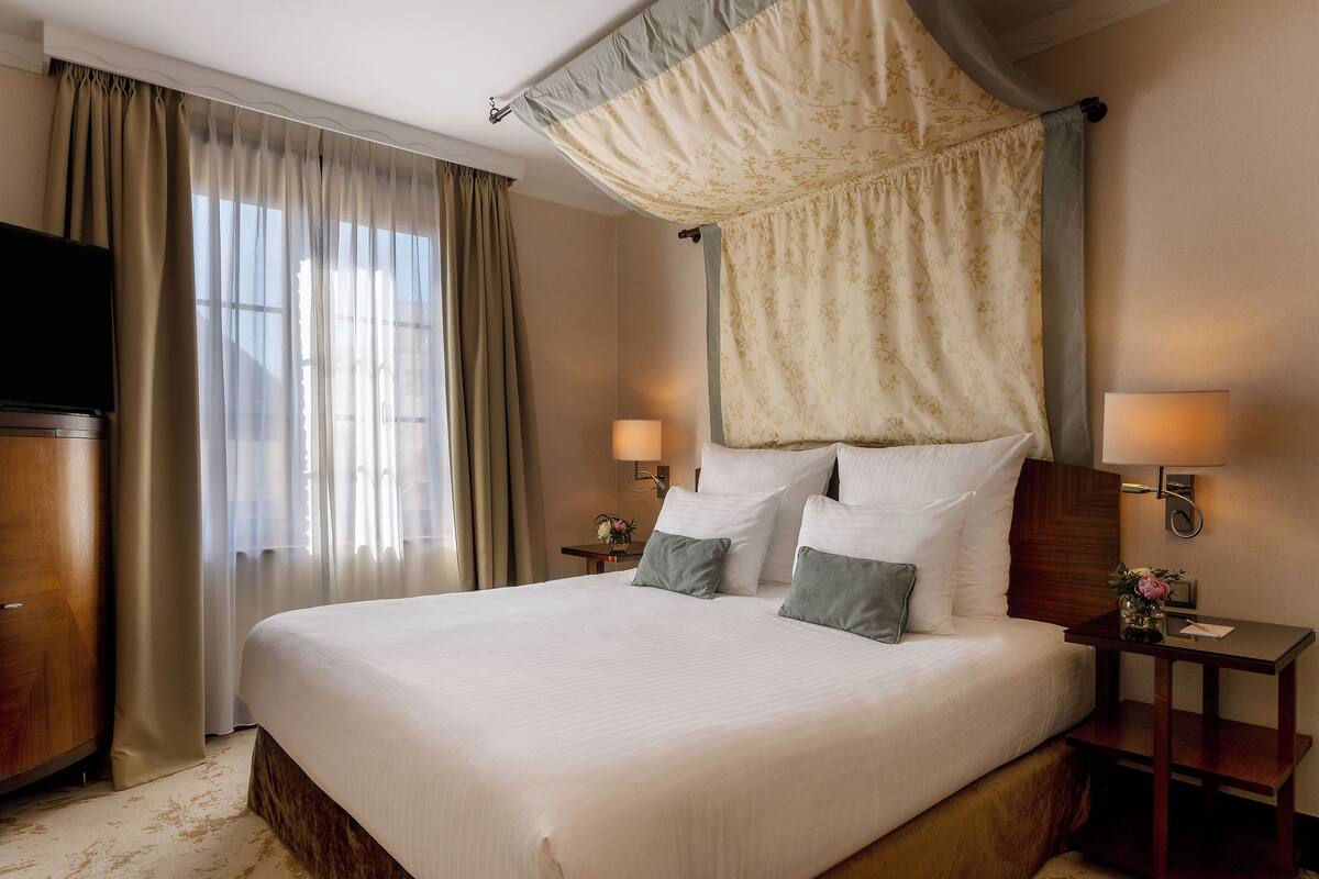 A hotel room with a large bed, a canopy, two bedside lamps, a nightstand, and a TV.