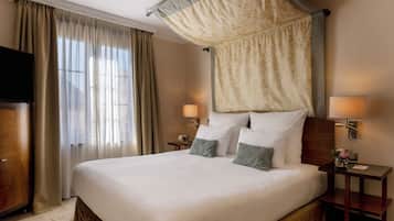 Habitación de hotel con una cama grande, dosel, dos lámparas de noche, mesitas de noche y televisor.