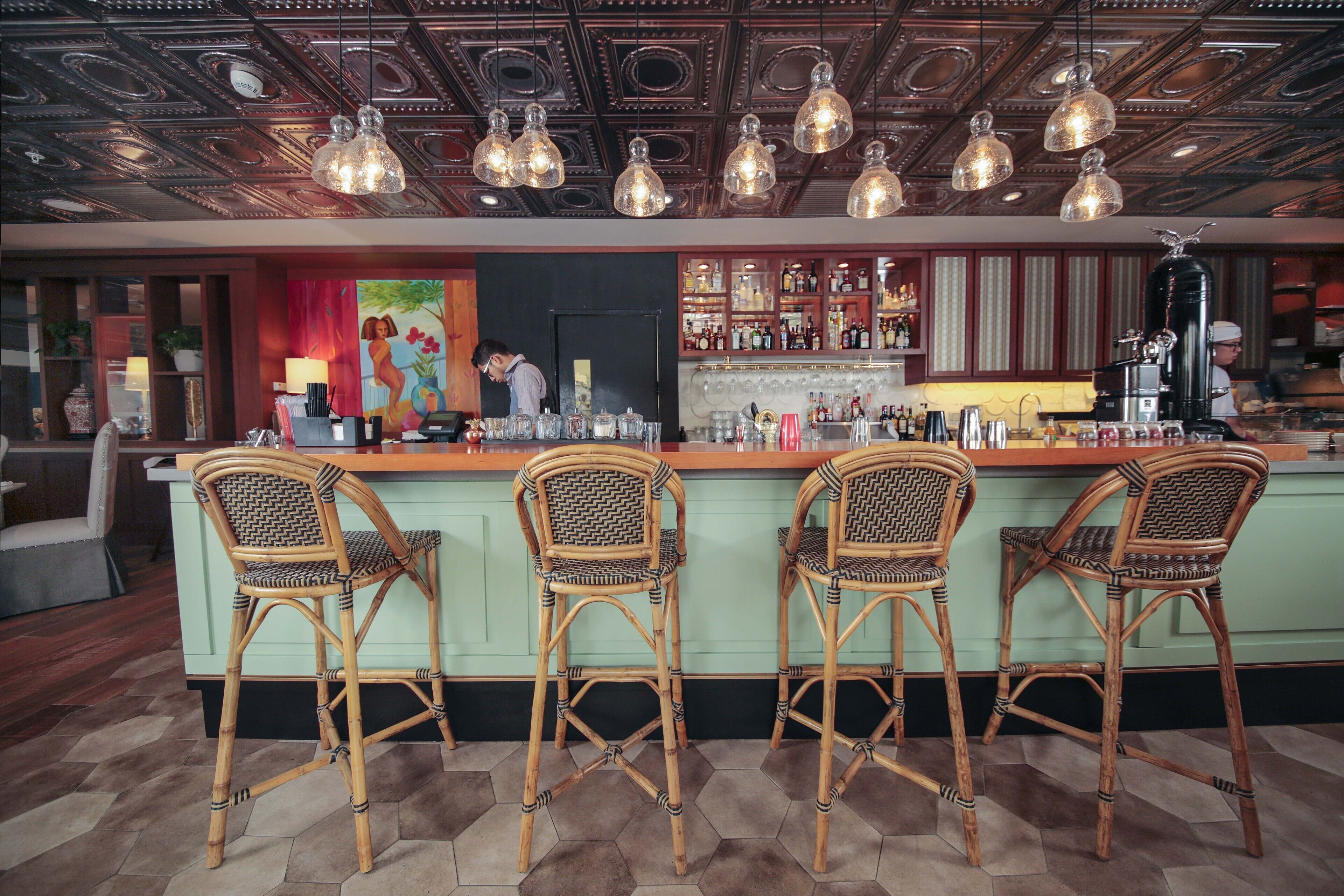A bar area with a green bar counter, wicker bar stools, and a ceiling with ornate patterns and hanging light fixtures.
