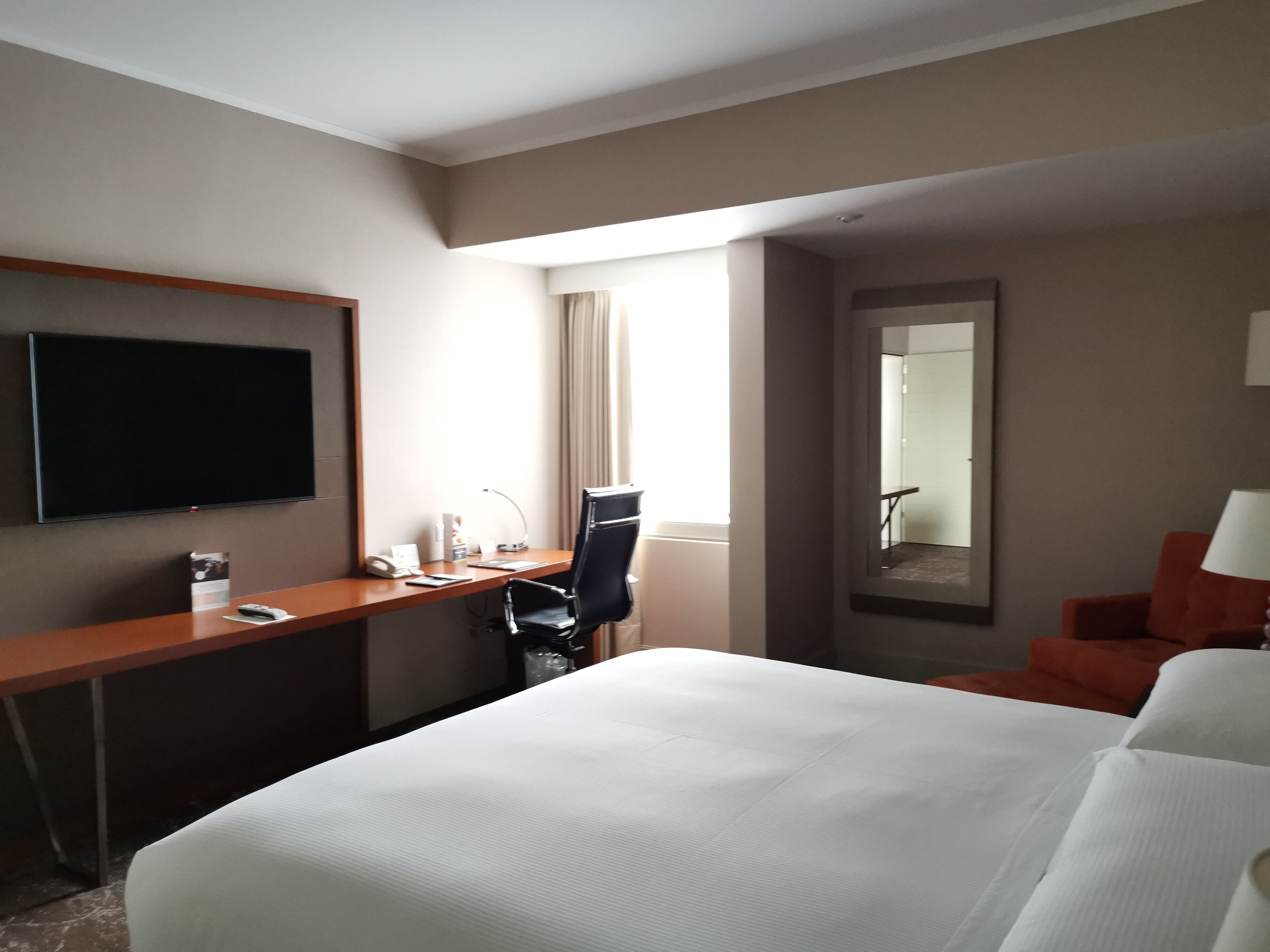 A hotel room with a bed, desk, chair, TV, and a window with curtains.