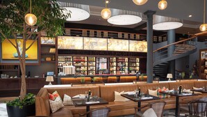 Un restaurante con zona de bar, asientos con mesas y sillas, y una escalera.