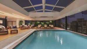 An indoor swimming pool with a glass ceiling, lounge chairs, and a view of the city at night. - El Pardo Lima - A DoubleTree by Hilton Hotel (Lima)