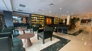 A modern lobby with green chairs, round tables, and a bar area. - El Pardo Lima - A DoubleTree by Hilton Hotel (Lima)