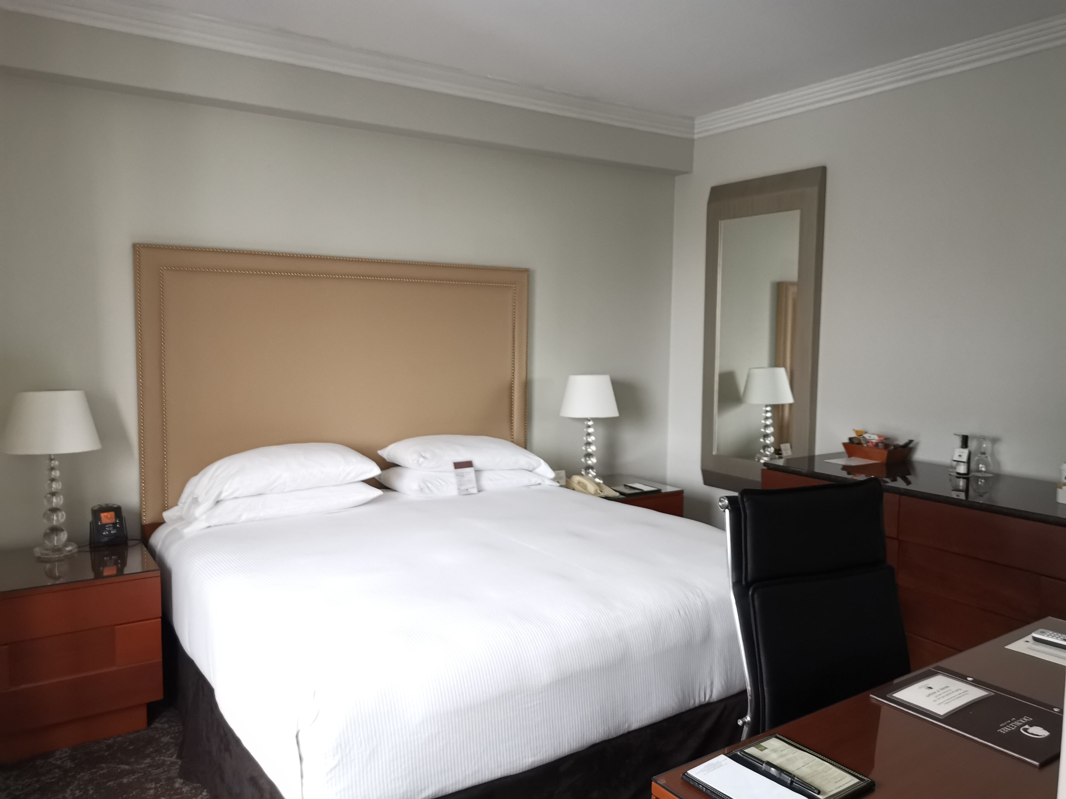 A hotel room with a large bed, two bedside lamps, a desk with a chair, a mirror, and a dresser.