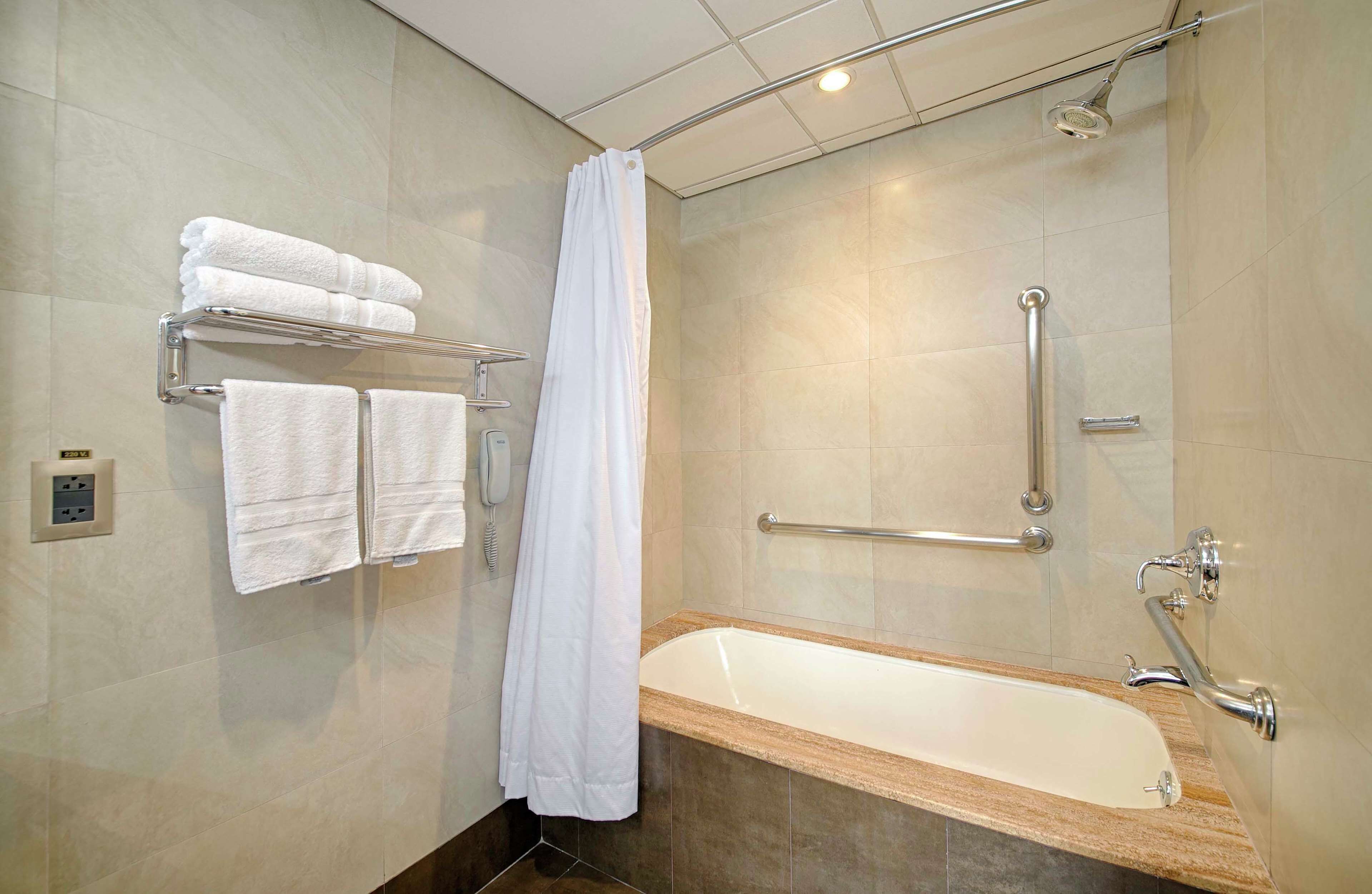 A modern bathroom with a bathtub, a shower with a handheld showerhead, and a towel rack with folded towels.