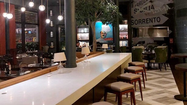 A modern bar area with a long counter, multiple stools, and hanging light fixtures. - El Pardo Lima - A DoubleTree by Hilton Hotel (Lima)