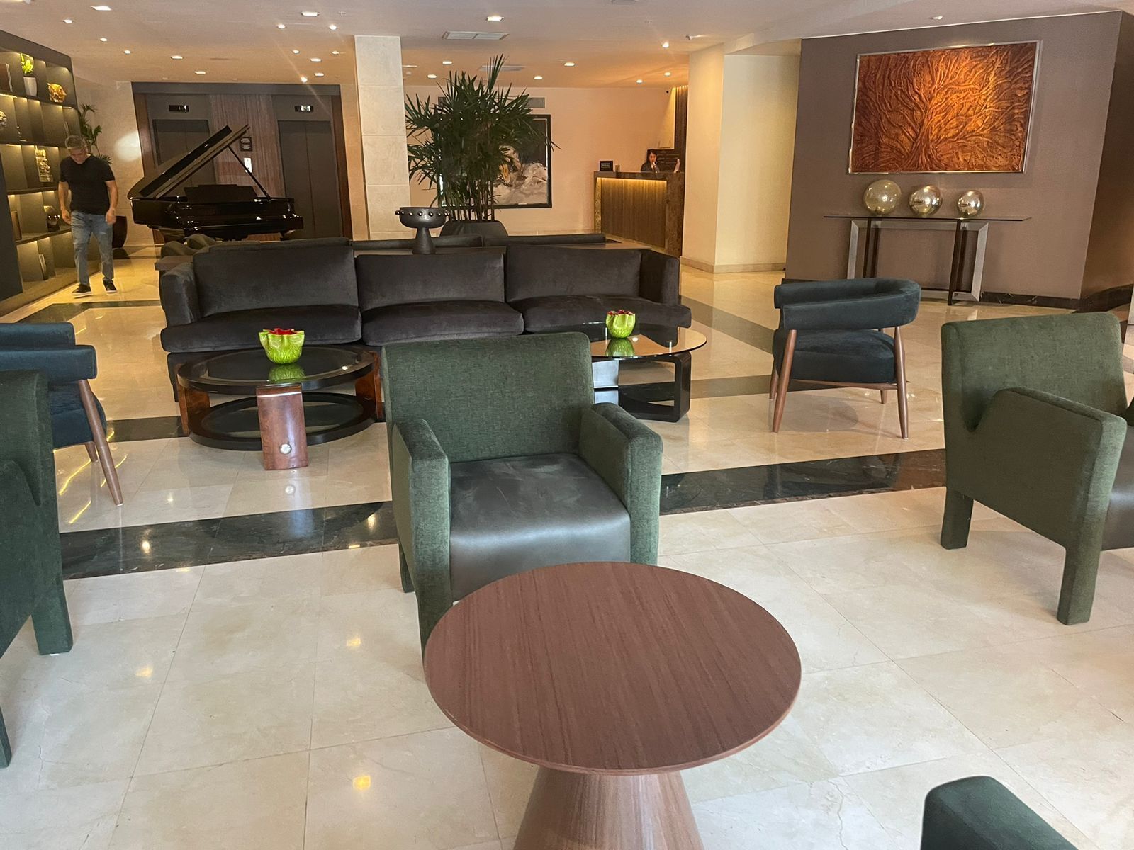 A modern lobby with a grand piano, comfortable seating, a reception desk, and a large decorative wall piece.
