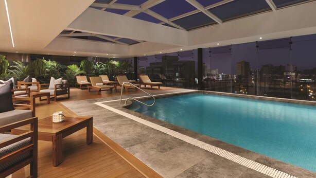 Un área de piscina interior moderna con sillones de descanso y vista a la ciudad de noche.