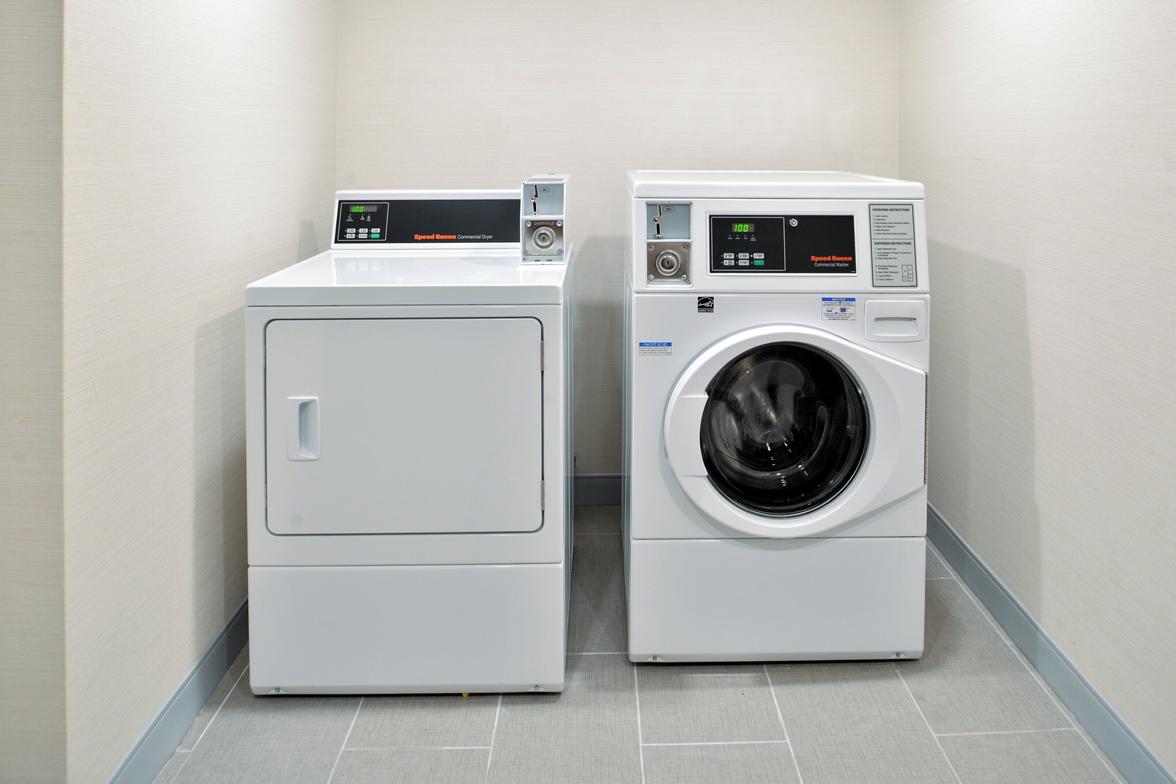 A commercial laundry facility with two machines, one dryer and one washer, in a tiled room.