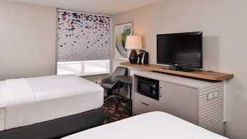 A hotel room with two beds, a desk with a television, a chair, and a window with patterned curtains.