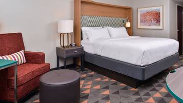 A hotel room with a bed, a red armchair, a small table, and a round ottoman.