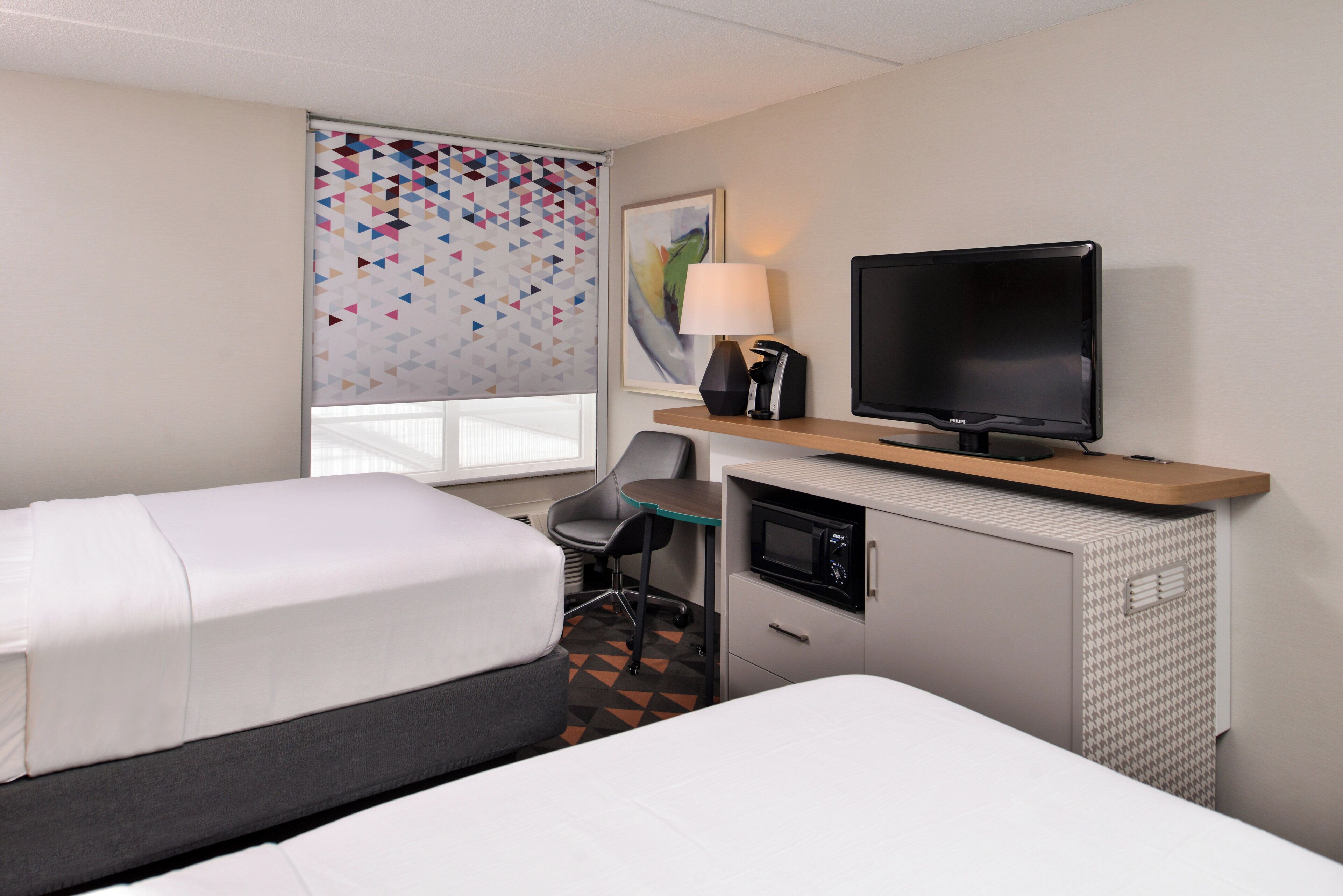 A hotel room with two beds, a desk with a television, a lamp, and a microwave.