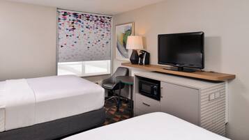 A hotel room with two beds, a desk with a television, a lamp, and a microwave.