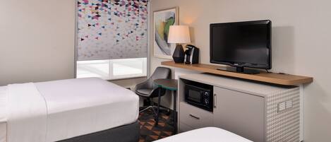 A hotel room with two beds, a desk with a television, a lamp, and a microwave.