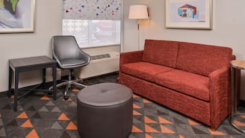 A room with a red sofa, a grey chair, a small table, and a round ottoman.