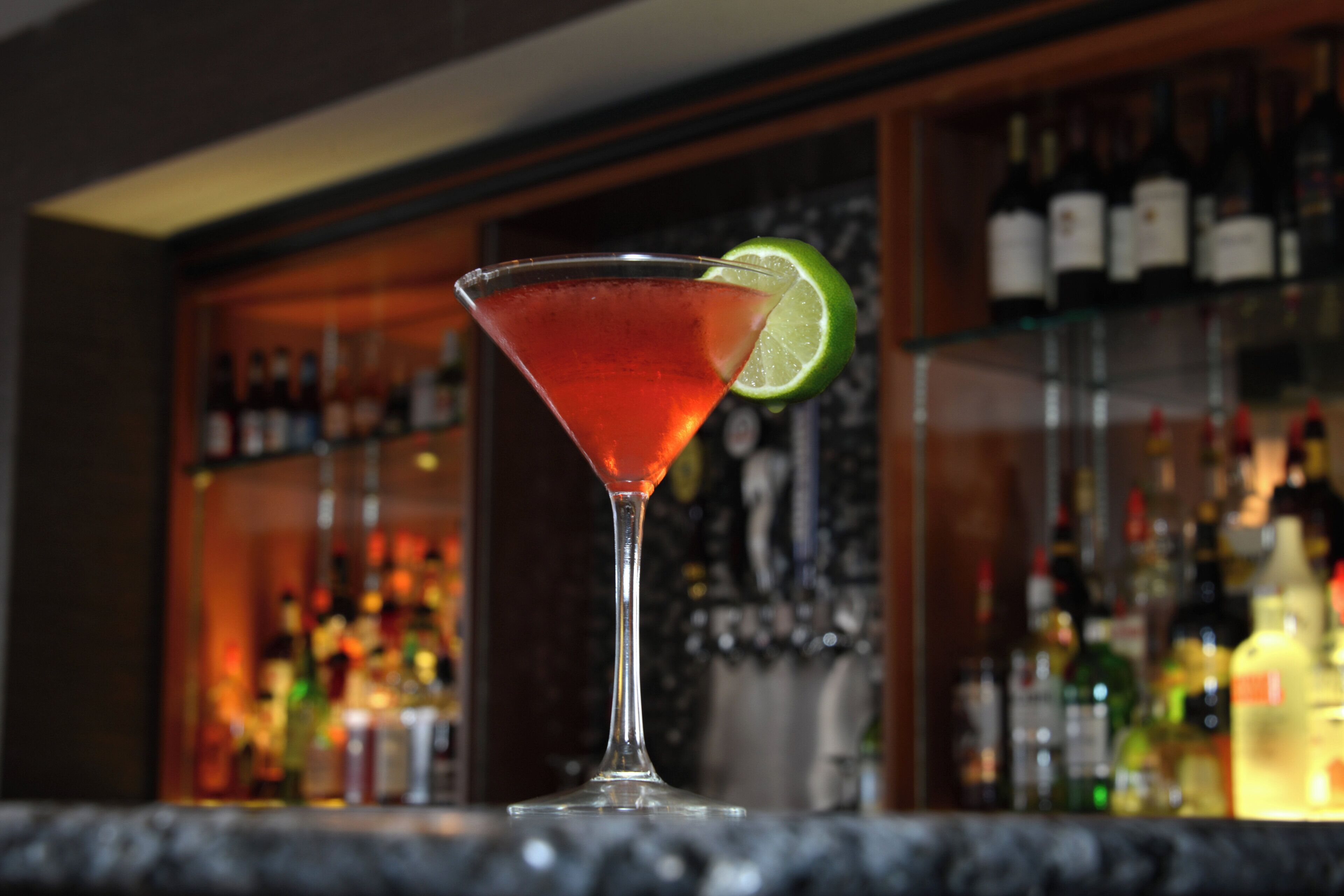 A martini glass with a lime garnish on a bar counter.