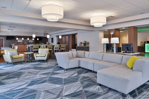 Un moderno vestíbulo de hotel con un sofá modular, sillones, zona de bar y alfombra estampada.