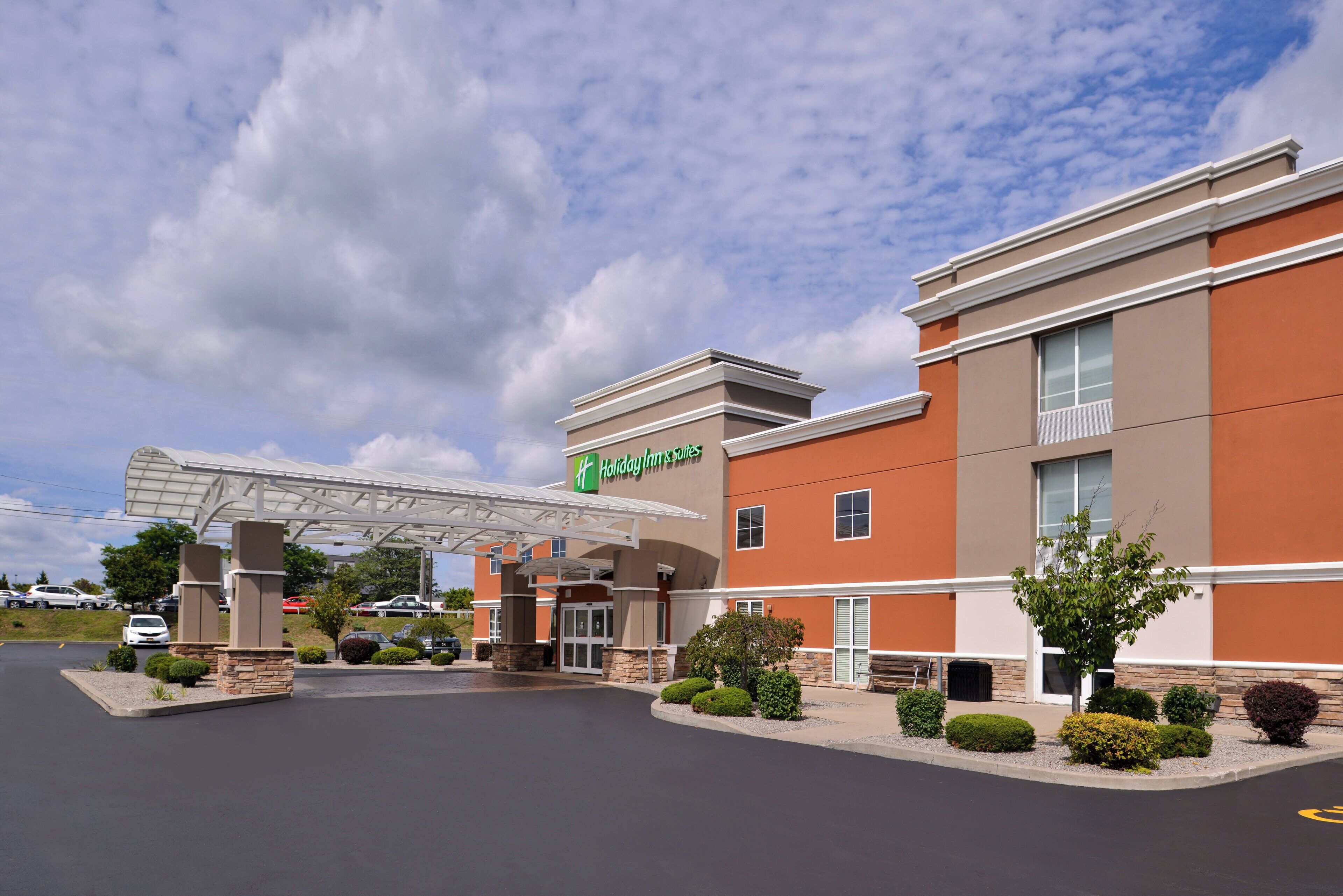 Un hôtel Holiday Inn & Suites doté d’une entrée abritée, d’un parking et offrant une vue sur un ciel dégagé.