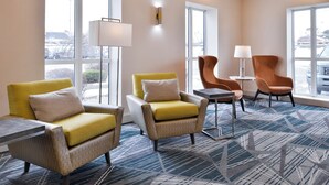 A hotel lobby with seating arrangements, a lamp, and large windows.