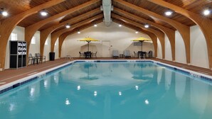 An indoor swimming pool with wooden beams, two sun umbrellas, and lounge chairs.