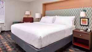 A hotel room with a large bed, a wooden headboard, a nightstand with a phone, and a wall-mounted lamp.