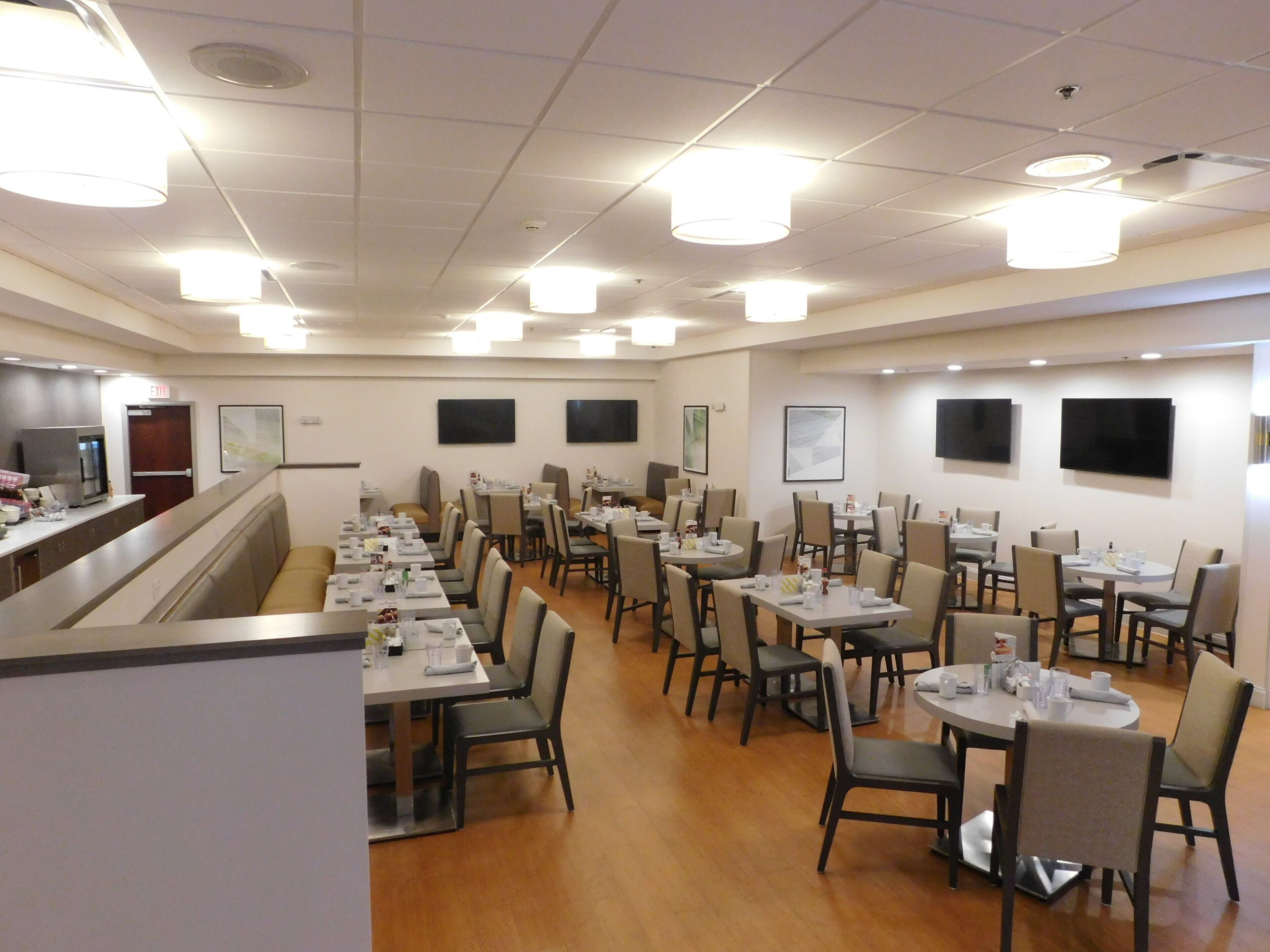 A spacious dining area with multiple tables and chairs, a counter with a cash register, and ceiling-mounted lights.