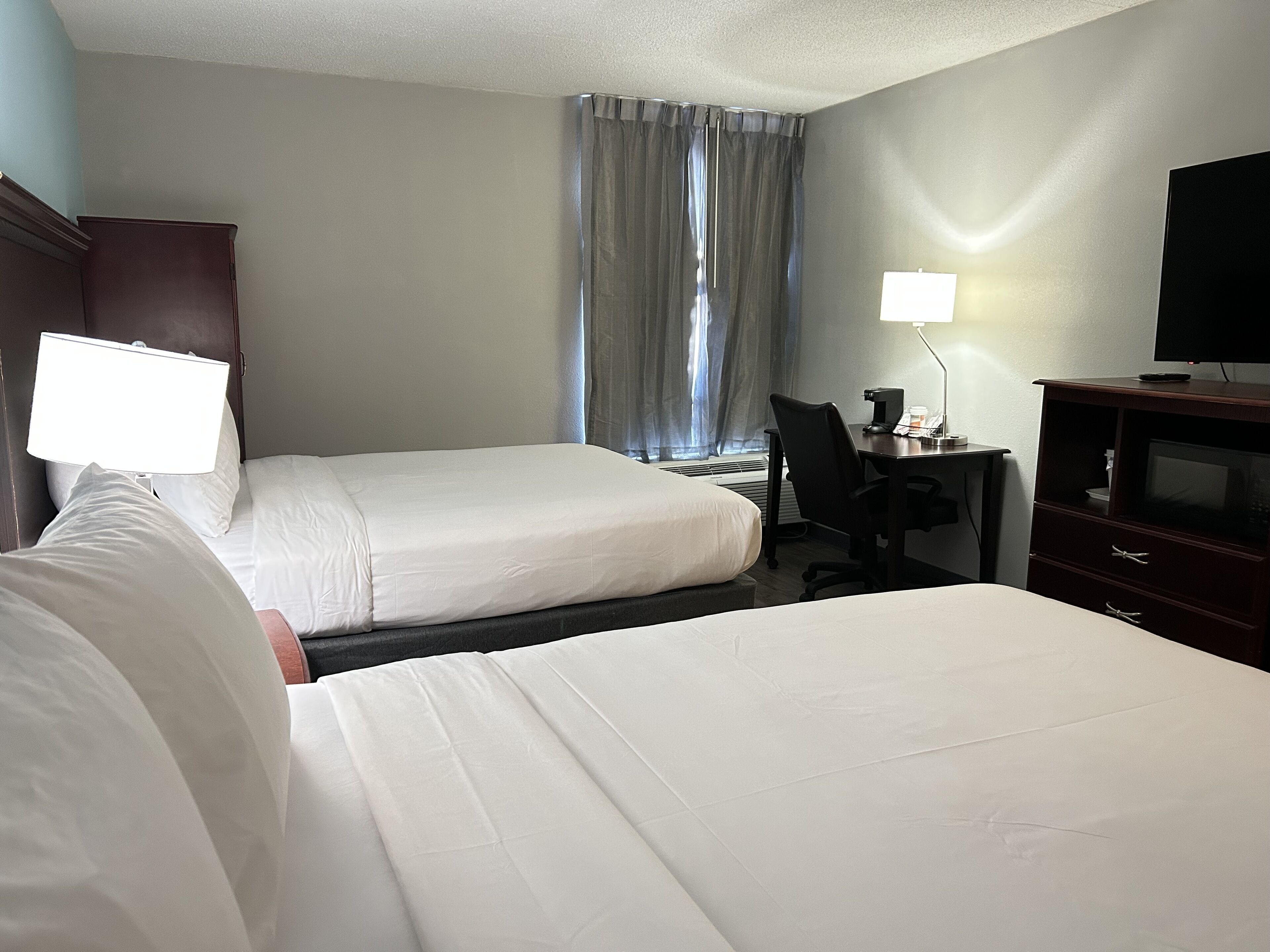 Habitación de hotel con dos camas, un escritorio con silla, televisor y ventana con cortinas.
