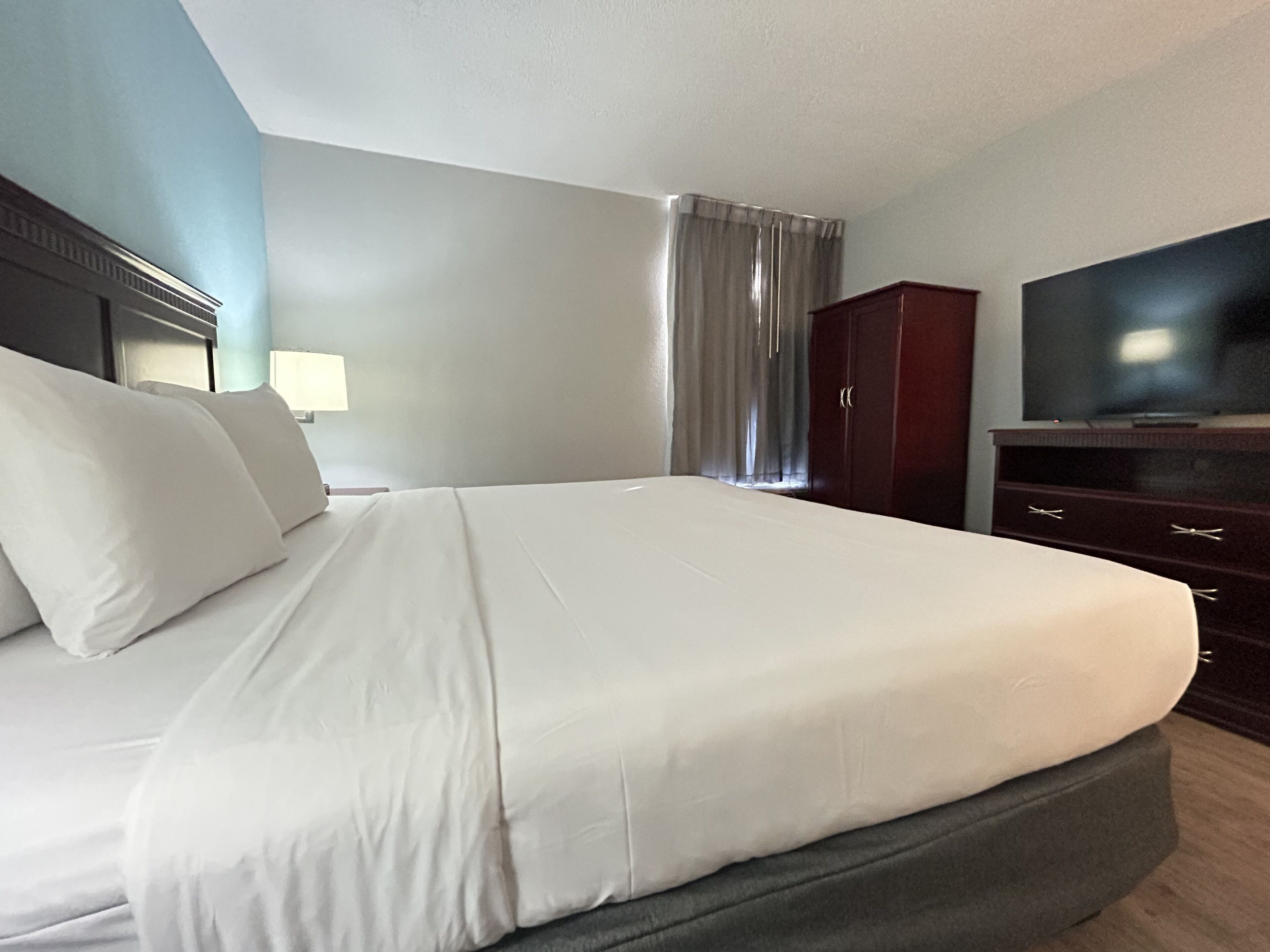 Habitación de hotel con una cama grande, televisión, armario y ventana con cortinas.