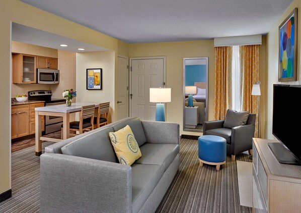 A hotel room with a living area, kitchenette, and a bedroom visible through a door.