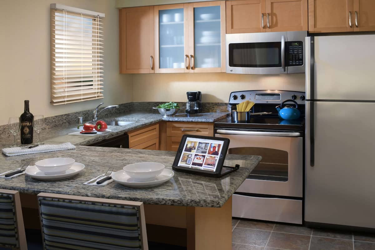 A modern kitchen with granite countertops, stainless steel appliances, wooden cabinets, and a tablet displaying recipes.