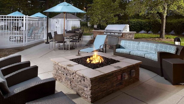An outdoor patio with a stone fire pit, wicker furniture, and a barbecue grill.