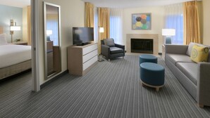 A hotel room with a bed, a television, a sofa, a chair, a fireplace, and a coffee table.
