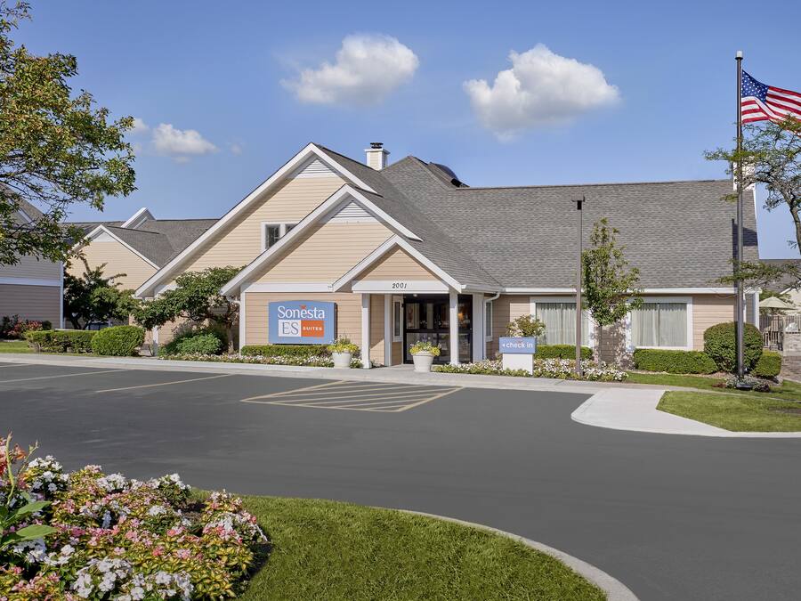 A Sonesta ES Suites hotel with a parking lot, a flag, and well-maintained landscaping.