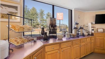 A kitchen area with a buffet setup, including bread, pastries, and coffee-making equipment.