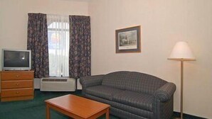 A hotel room with a sofa, a wooden table, a television on a dresser, a framed picture on the wall, and a floor lamp. - Econo Lodge Hendersonville (Hendersonville)